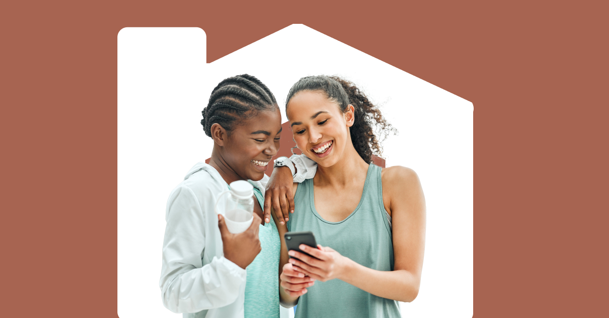 Two young women smiling together while looking at a phone.