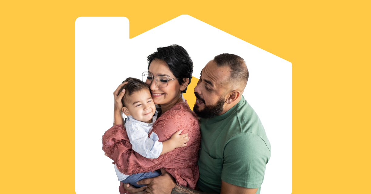 A woman holding a child while a man makes a silly face towards the child behind her.